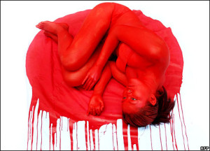 Image depicts a woman in a fetal position drenched in fake blood.