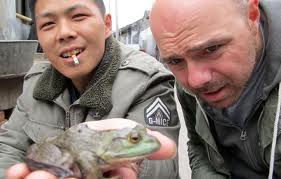 Screenshot from "An Idiot Abroad," Pilkington examines a live frog in the hand of a Chinese man