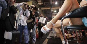 Male photographers at a pornography convention photographing a woman with her legs spread