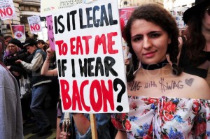Woman at SlutWalk protest holding sign that reads "Is it legal to eat me if I wear bacon?"
